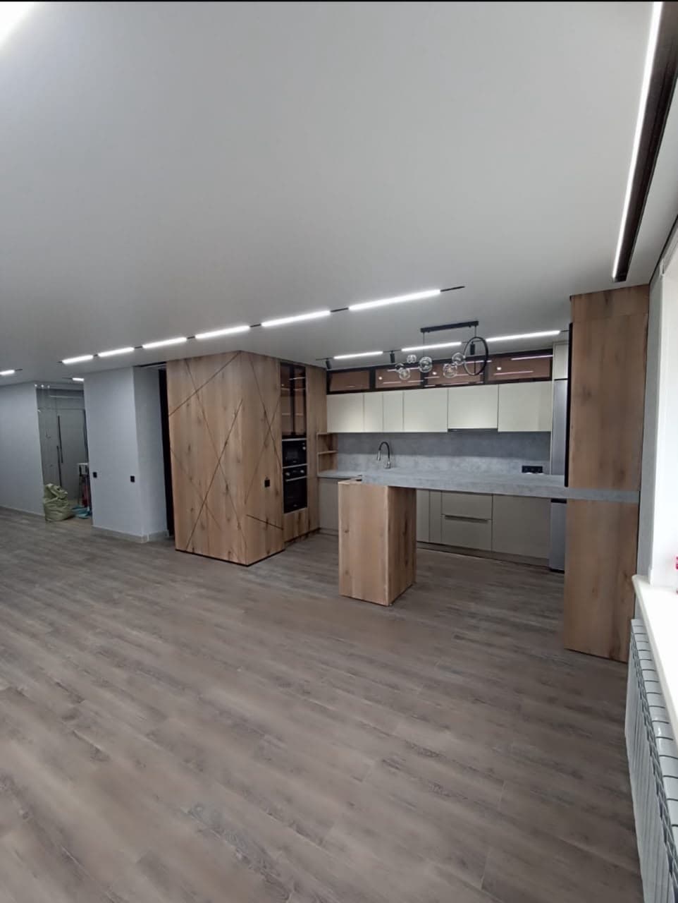 Minimalist open-plan kitchen with wood-grain cabinetry, concrete countertops, and recessed ceiling strip lighting.