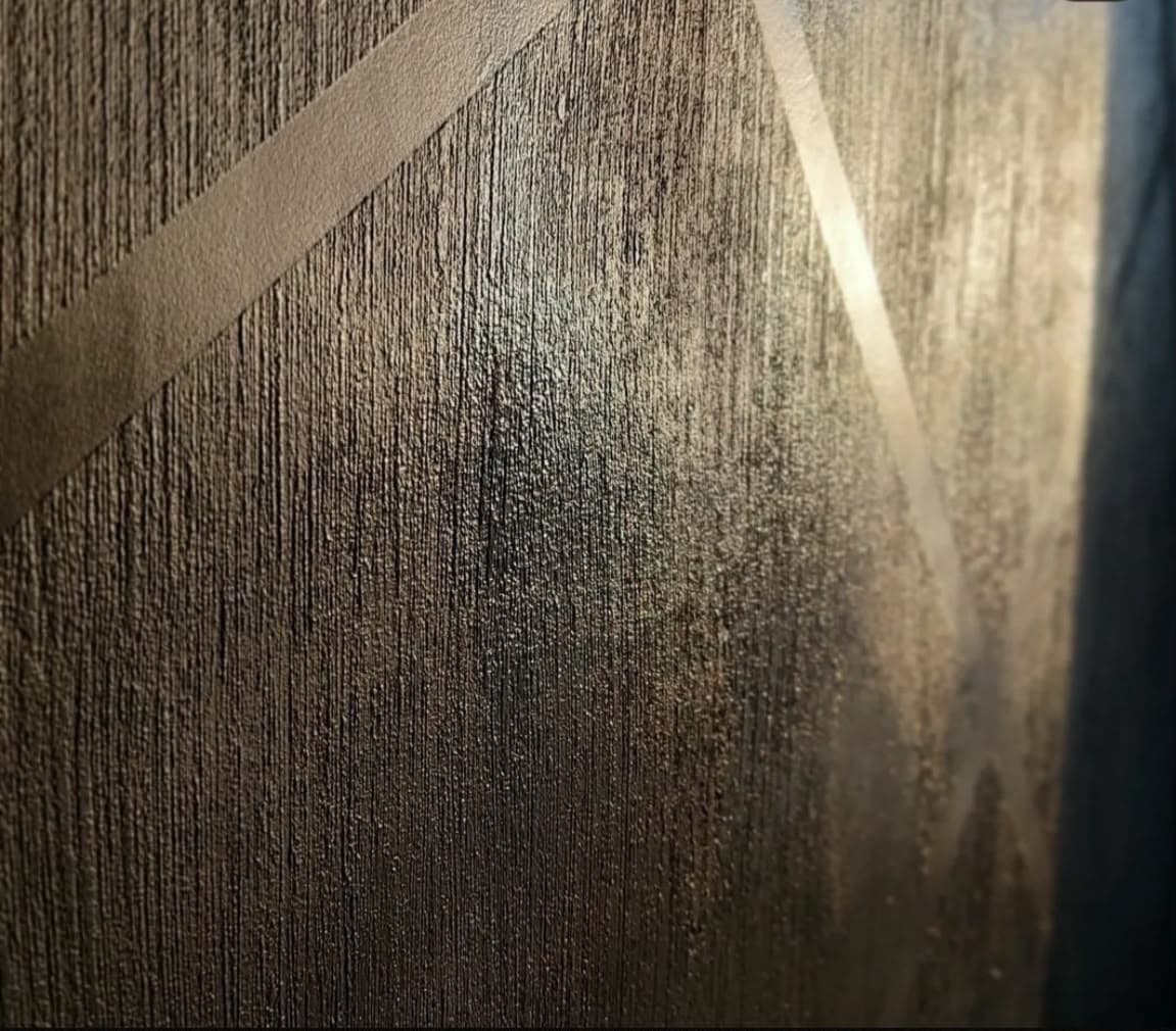 Textured bronze surface with vertical ridges and smooth diagonal geometric lines reflecting warm light.